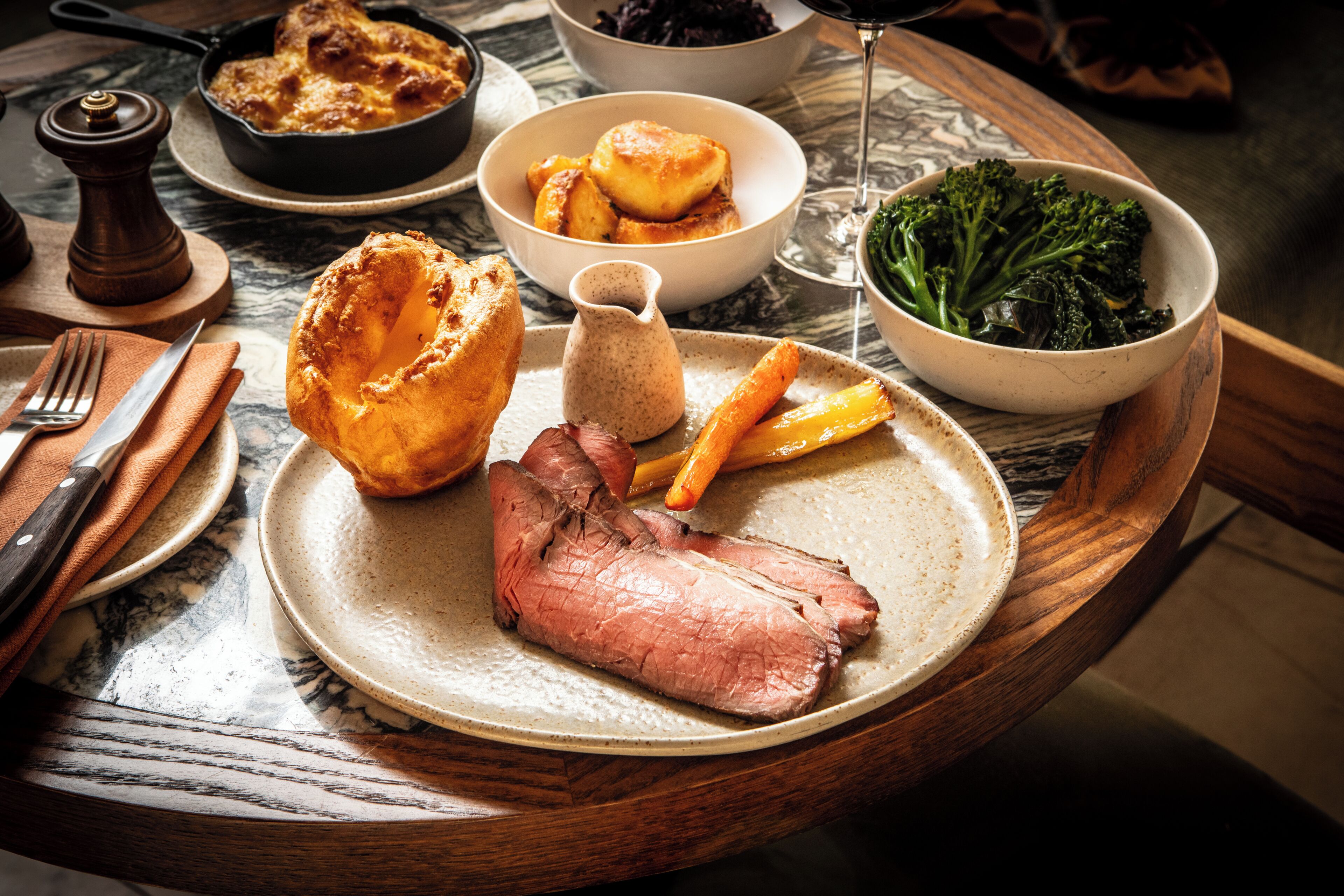 A plate with roast beef, Yorkshire pudding, and vegetables on a wooden table.