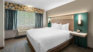 A hotel room with a large bed, a bedside table with a phone, a window with curtains, and a geometric-patterned wall.