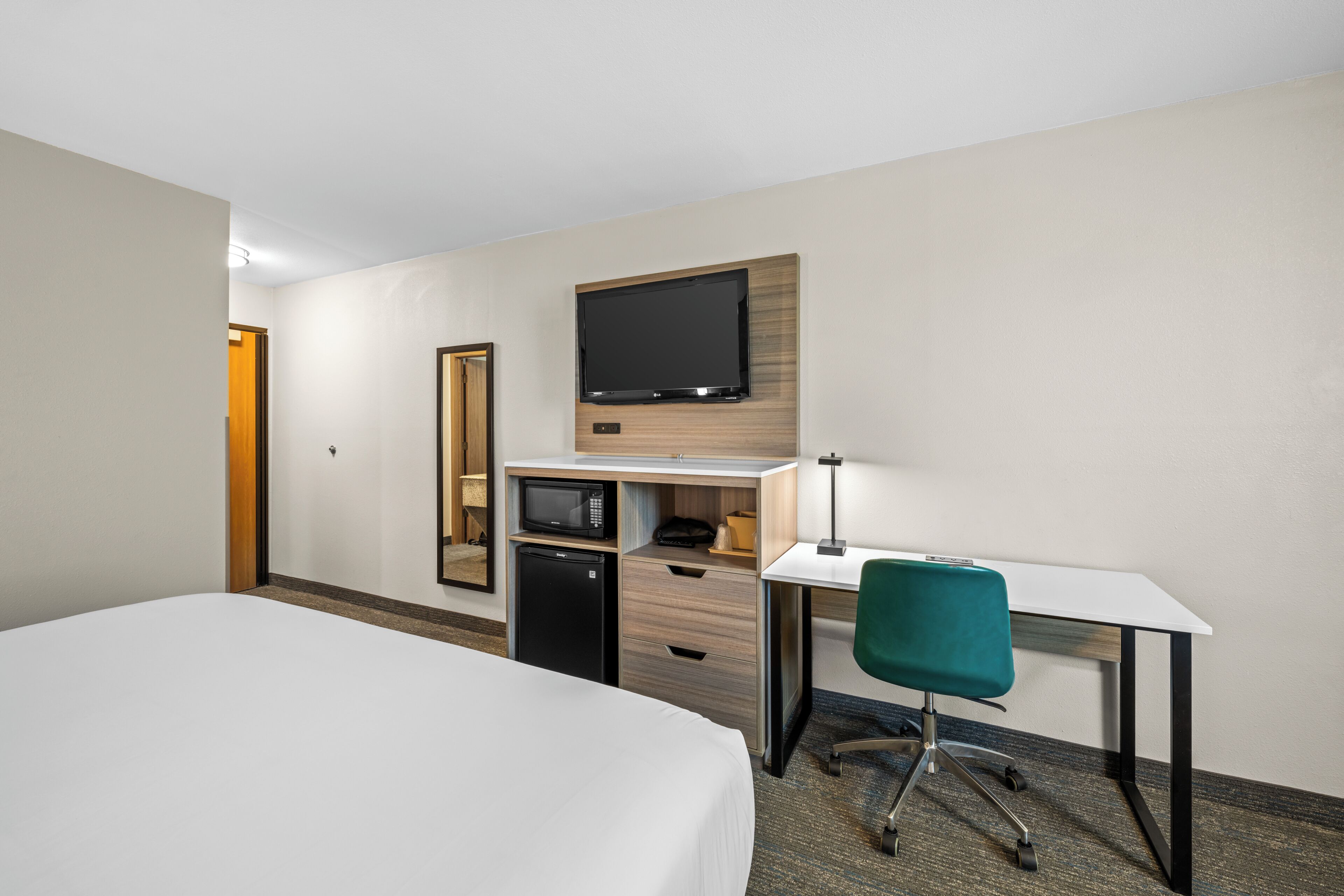 Una habitación de hotel con cama, escritorio, silla, microondas y televisión.