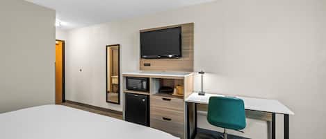 A hotel room with a bed, desk, chair, microwave, and television.