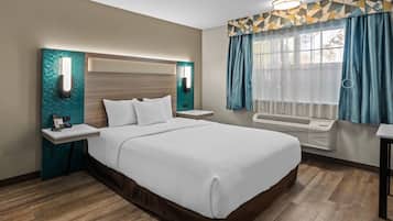 A hotel room with a large bed, a bedside table with a phone, a wall-mounted light, and a window with curtains.