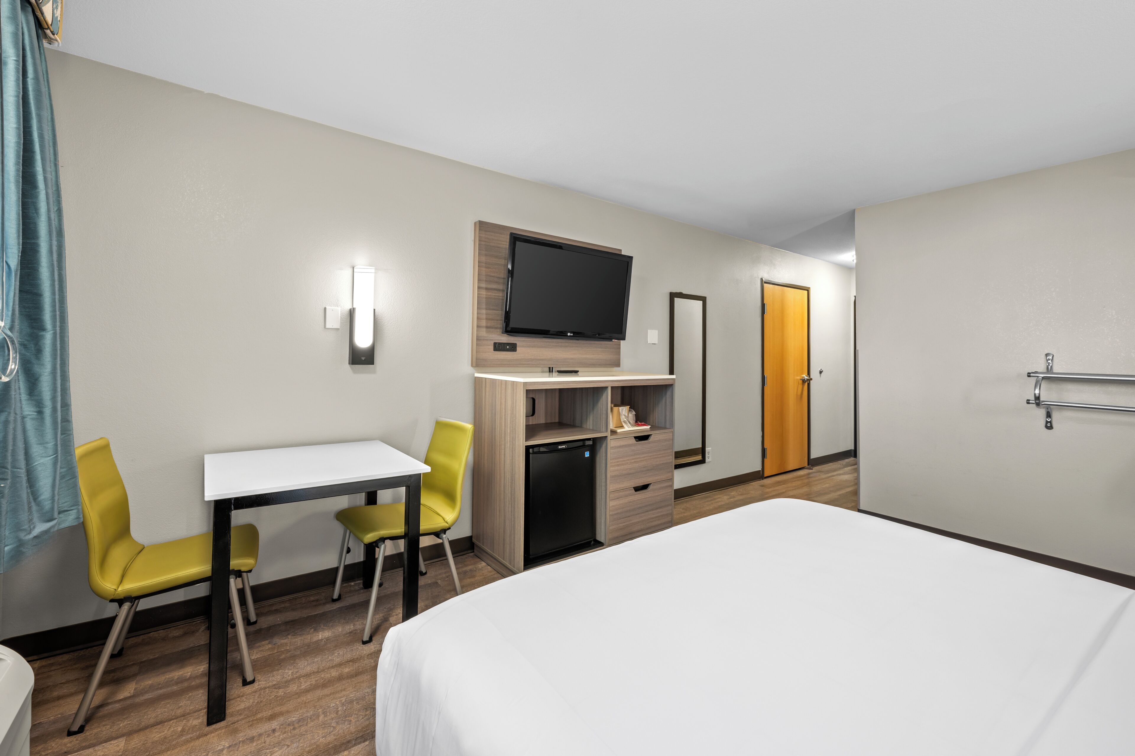 A hotel room with a bed, a desk, two chairs, a television, a wardrobe, and a door.