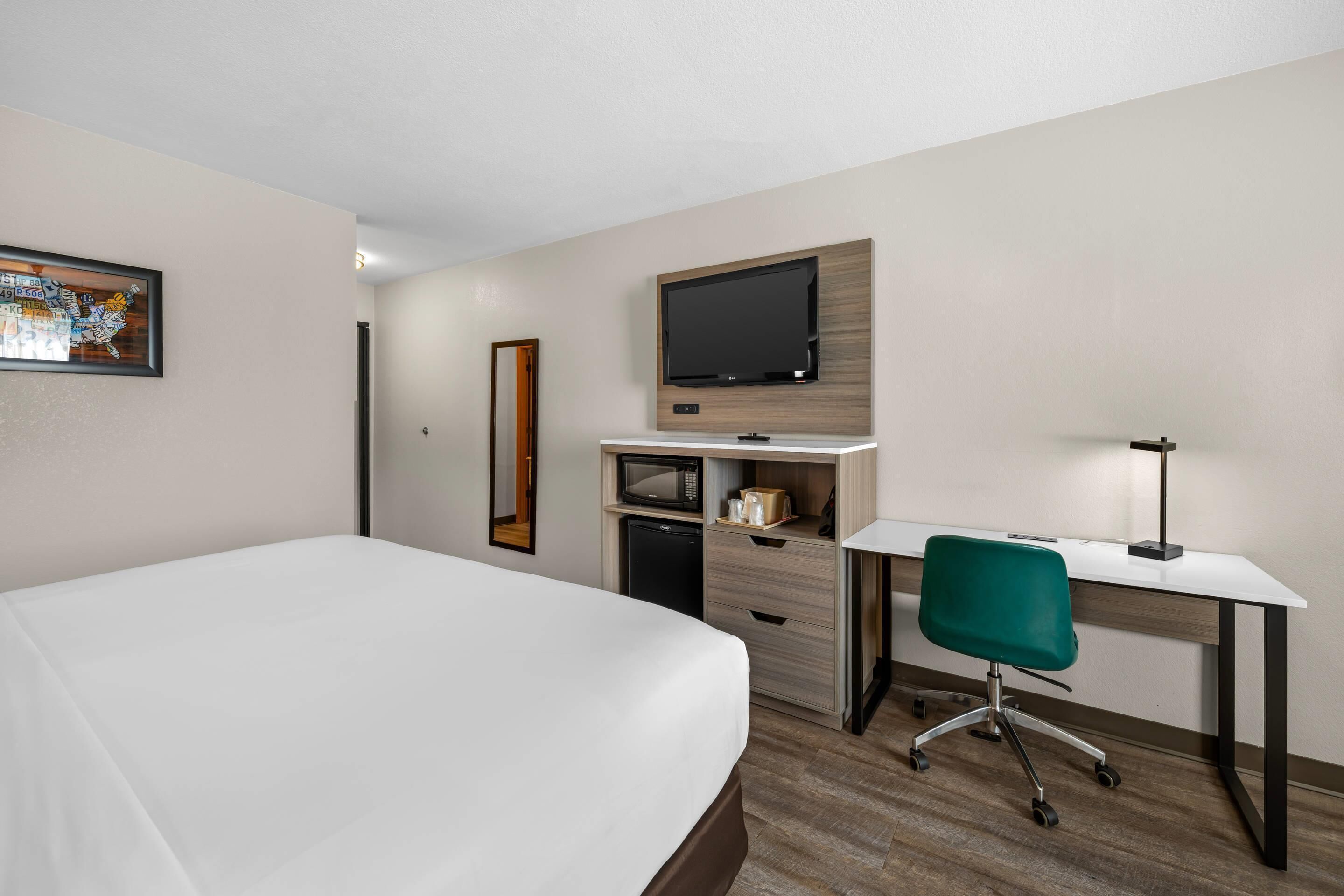 Une chambre d’hôtel équipée d’un lit, d’un bureau avec une chaise, d’une télévision, d’un four à micro-ondes et d’un petit réfrigérateur.
