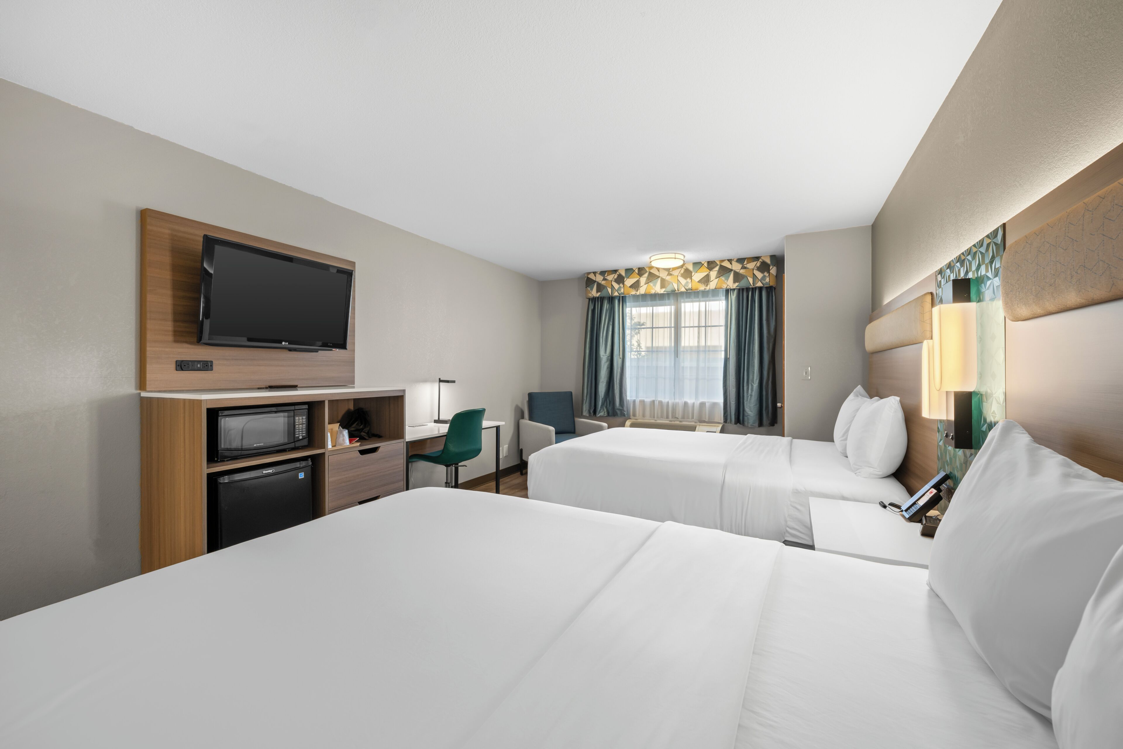 Ein Hotelzimmer mit zwei Betten, einem Fernseher, einem Schreibtisch mit Mikrowelle und einem Sessel.