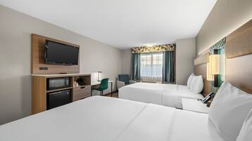 Ein Hotelzimmer mit zwei Betten, einem Fernseher, einem Schreibtisch mit Mikrowelle und einem Sessel.