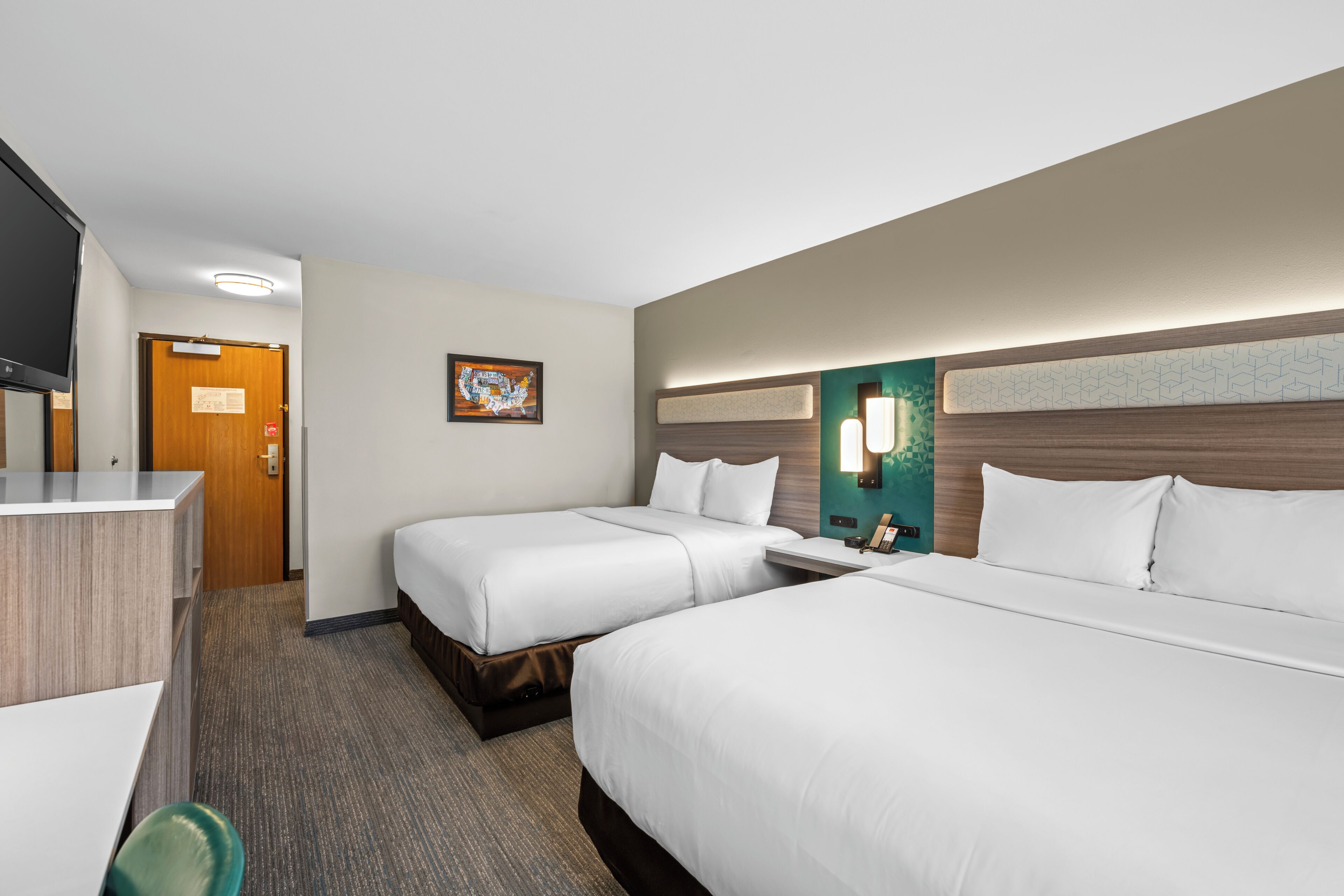 A hotel room with two beds, a desk, a chair, a TV, and a painting on the wall.