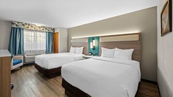A hotel room with two beds, a desk, and a window with curtains.