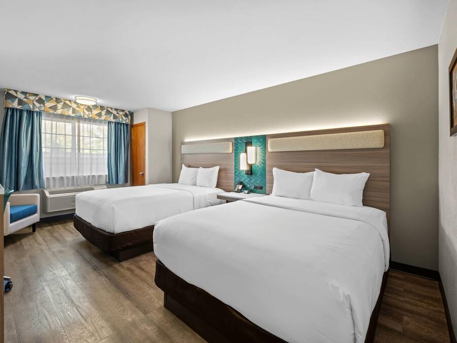 A hotel room with two beds, a desk, and a window with curtains.