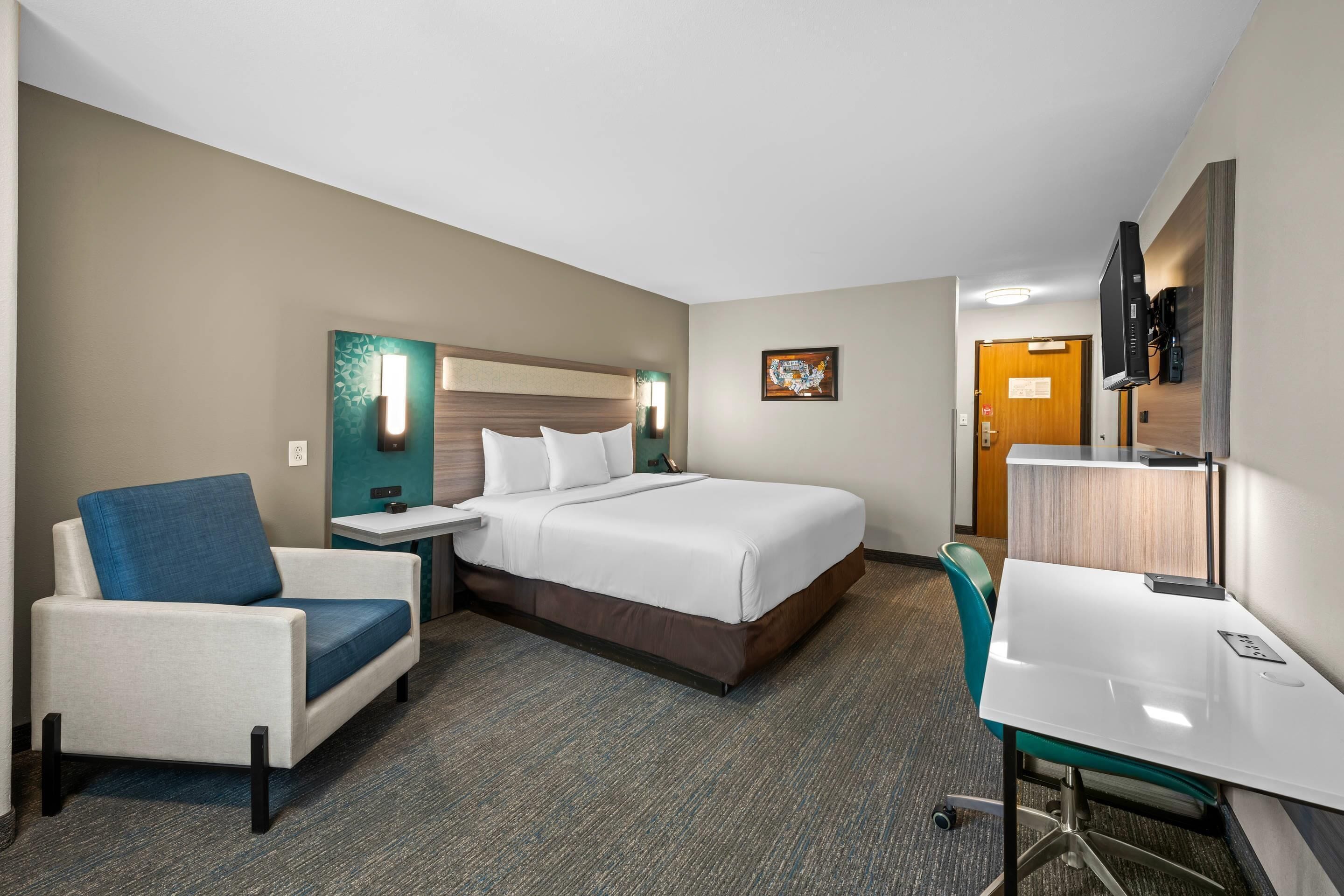 A hotel room with a bed, a desk, a chair, a nightstand, and a wall-mounted TV.