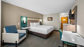 A hotel room with a bed, a desk, a chair, a nightstand, and a wall-mounted TV.