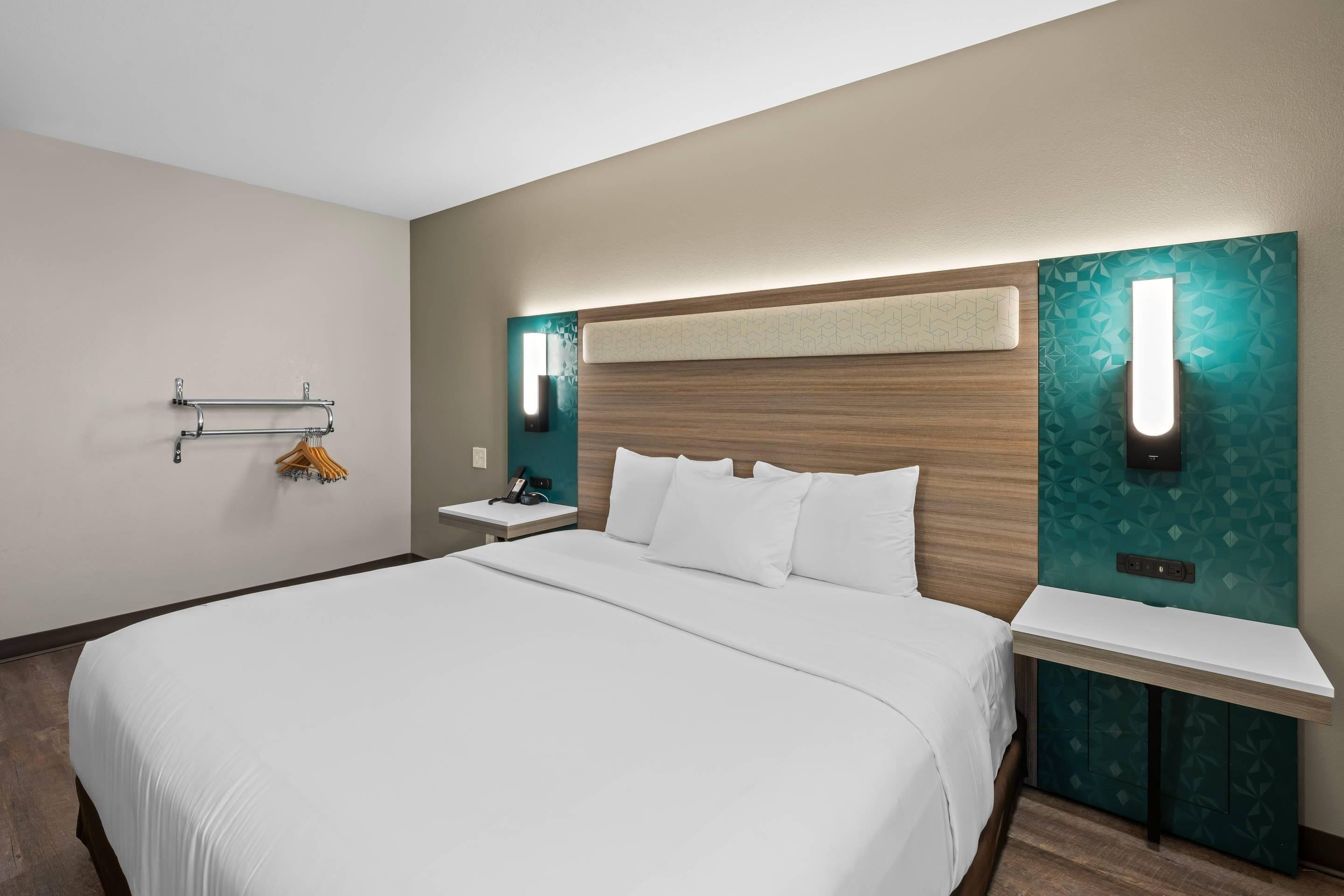 A hotel room with a large bed, bedside tables, a towel rack, and a wall-mounted light fixture.