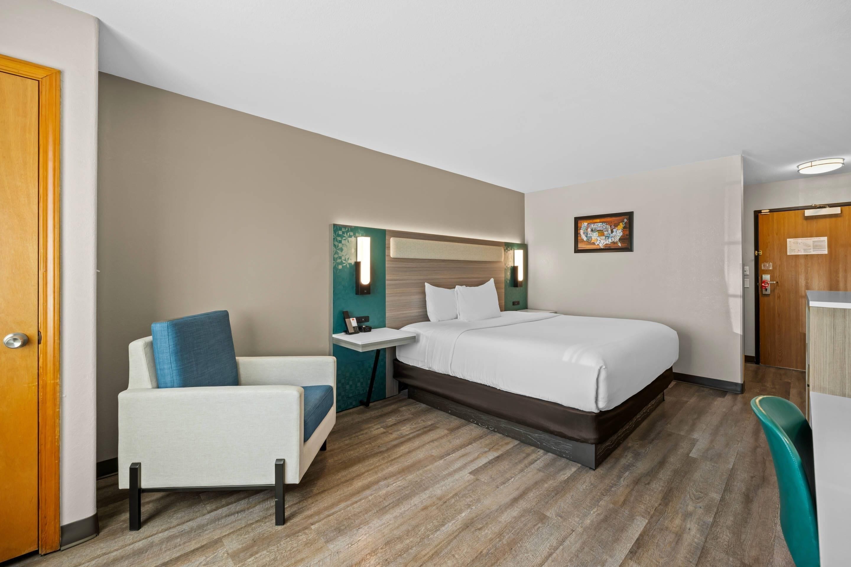 A hotel room with a bed, a chair, a small table, and a desk.