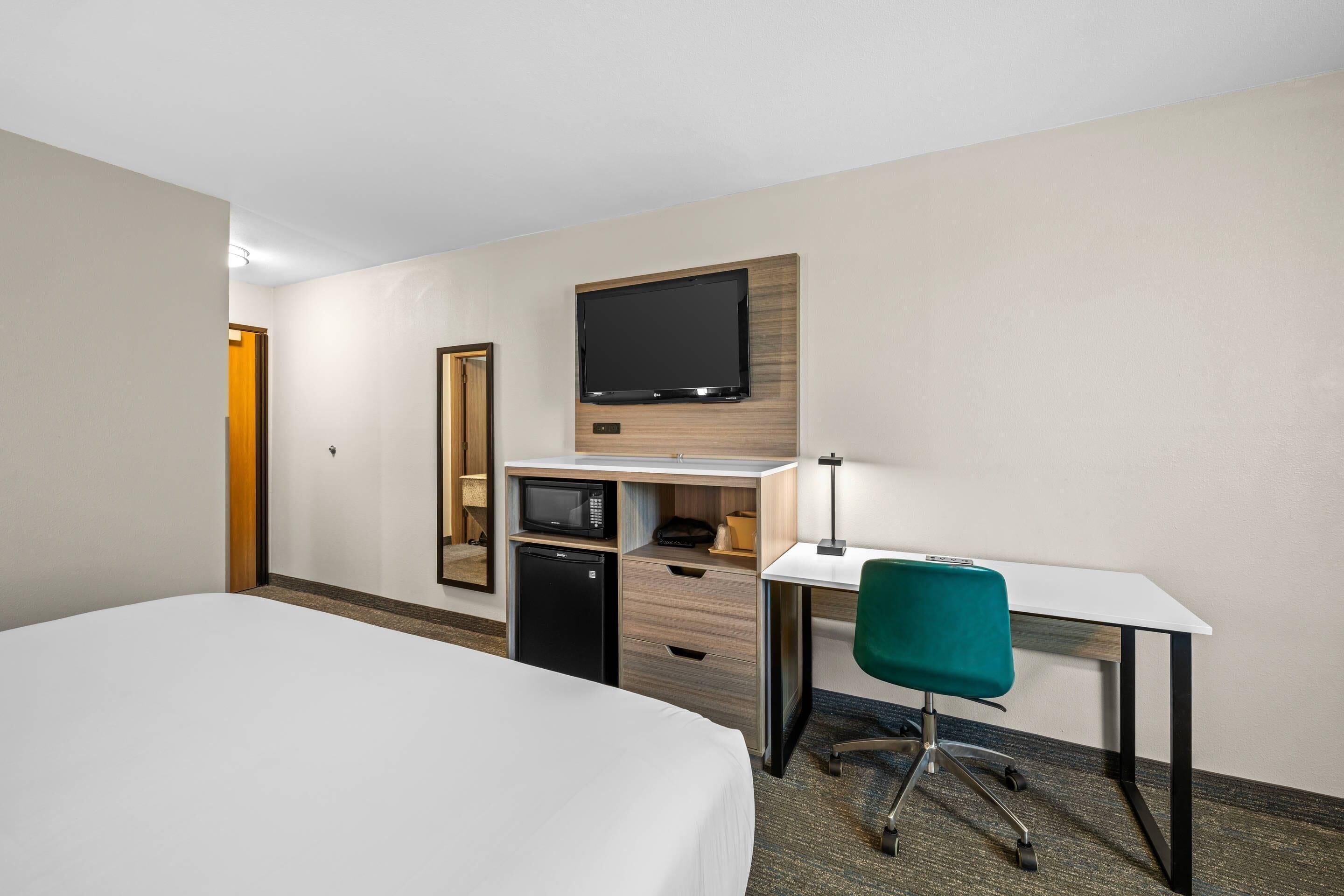 A hotel room with a bed, desk, chair, microwave, and TV.
