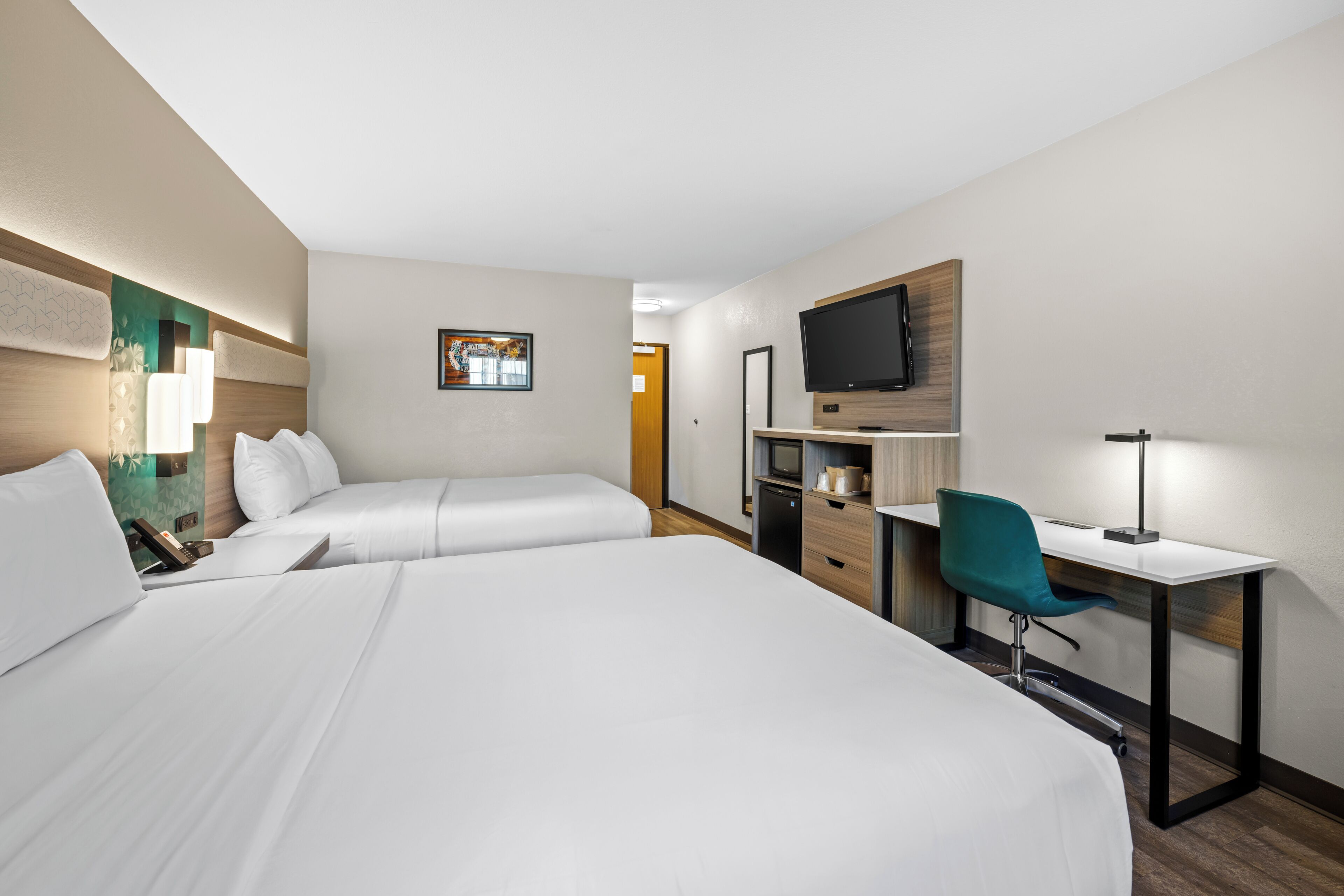 A hotel room with two beds, a desk, a chair, a TV, and a desk lamp.