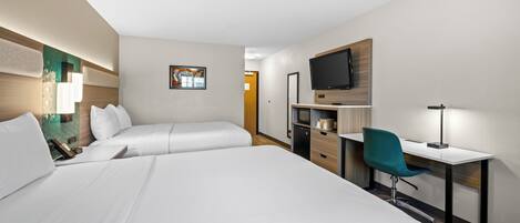 A hotel room with two beds, a desk, a chair, a TV, and a desk lamp.