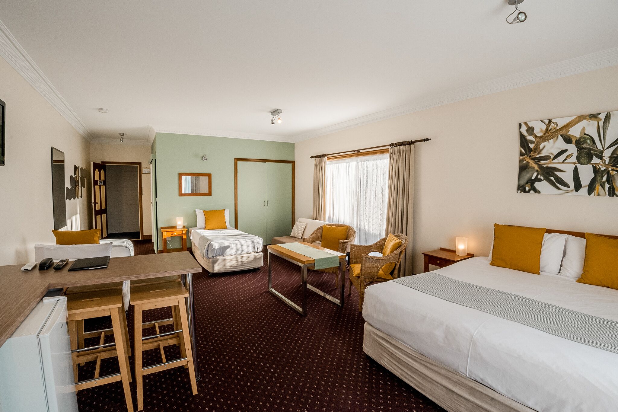 Une chambre d’hôtel avec un lit, un canapé, un bureau et une chaise. On y trouve une petite table et une table de chevet avec une lampe.