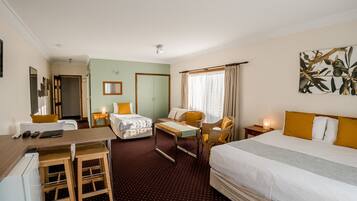 Une chambre d’hôtel avec un lit, un canapé, un bureau et une chaise. On y trouve une petite table et une table de chevet avec une lampe.