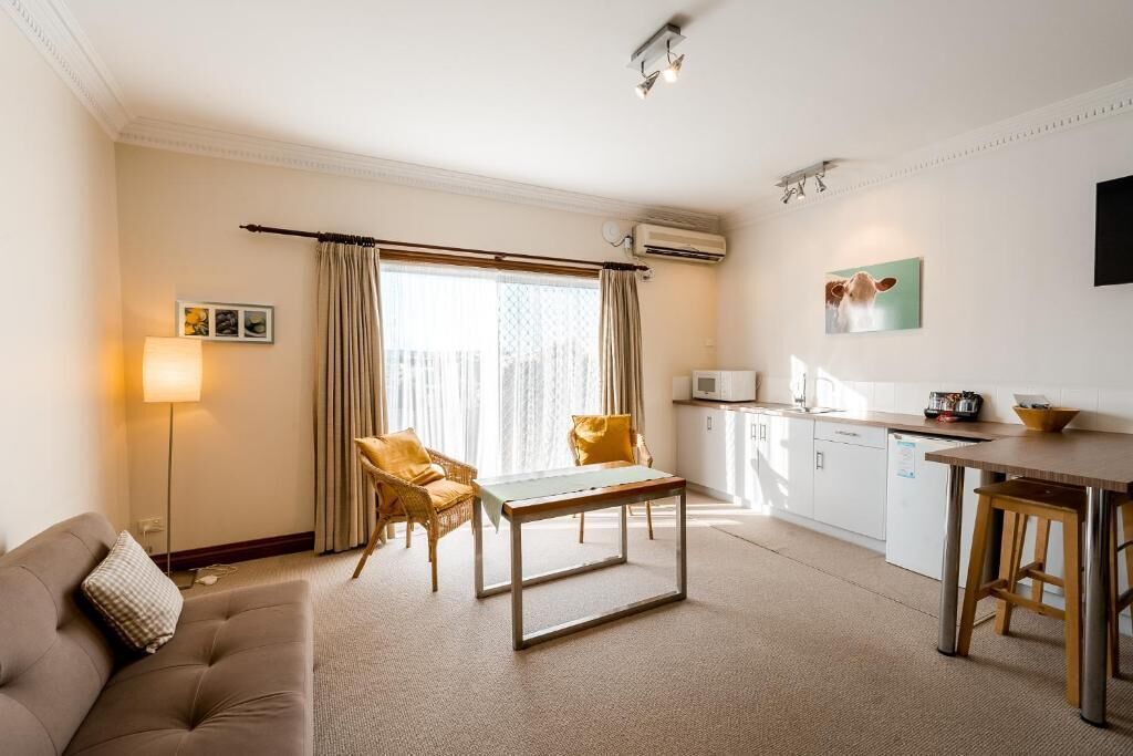 A hotel room with a sofa, a dining table, a kitchen area, and a window with curtains.