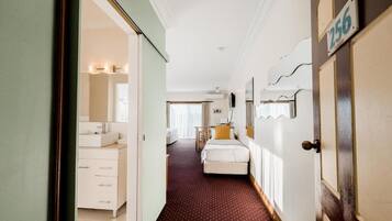 A hotel room with a bed, a desk, a chair, a window, and a bathroom with a sink and mirror.