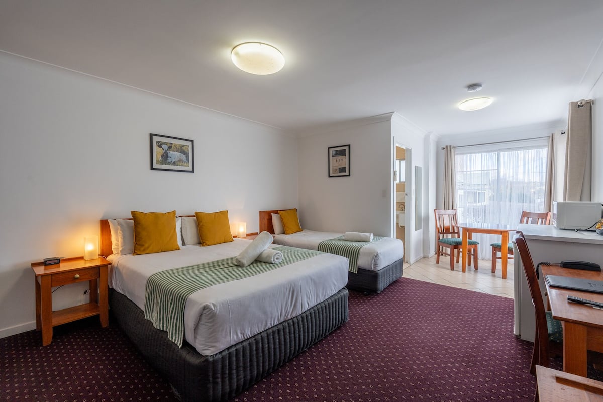 A hotel room with two beds, a desk, and a dining area.