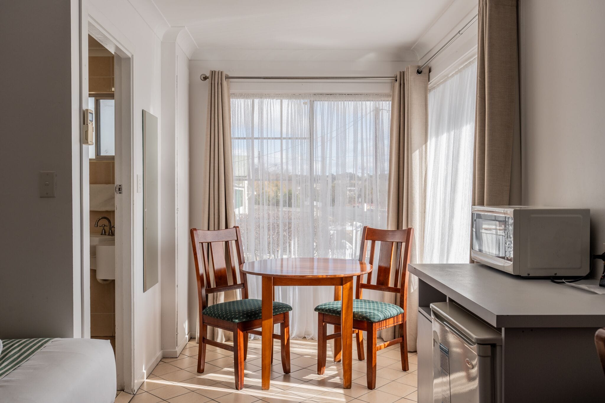 Una habitación de hotel compacta con una mesa de comedor y sillas, un microondas y una pequeña kitchenette.