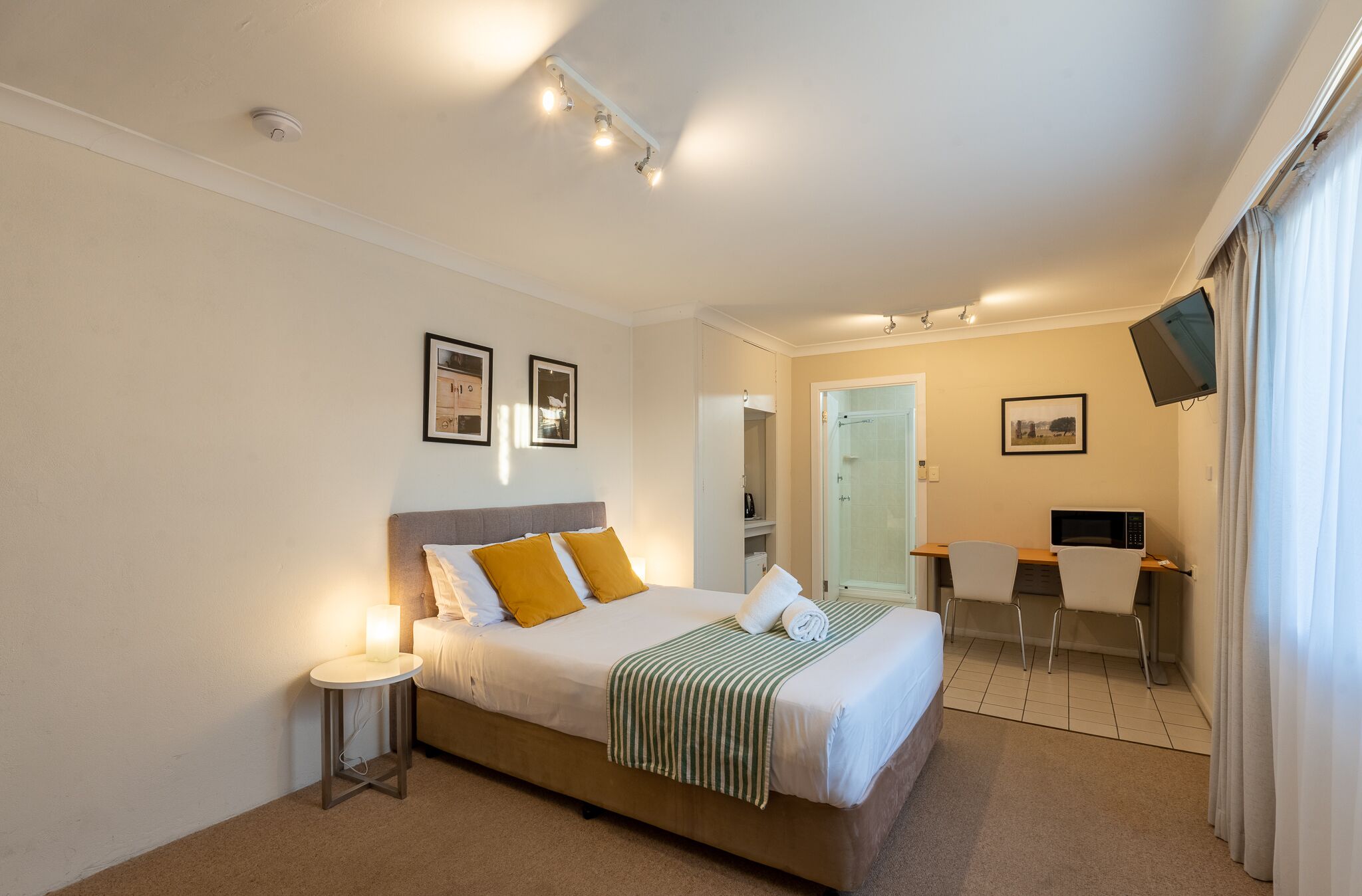A hotel room with a bed, bedside table, desk, and TV.