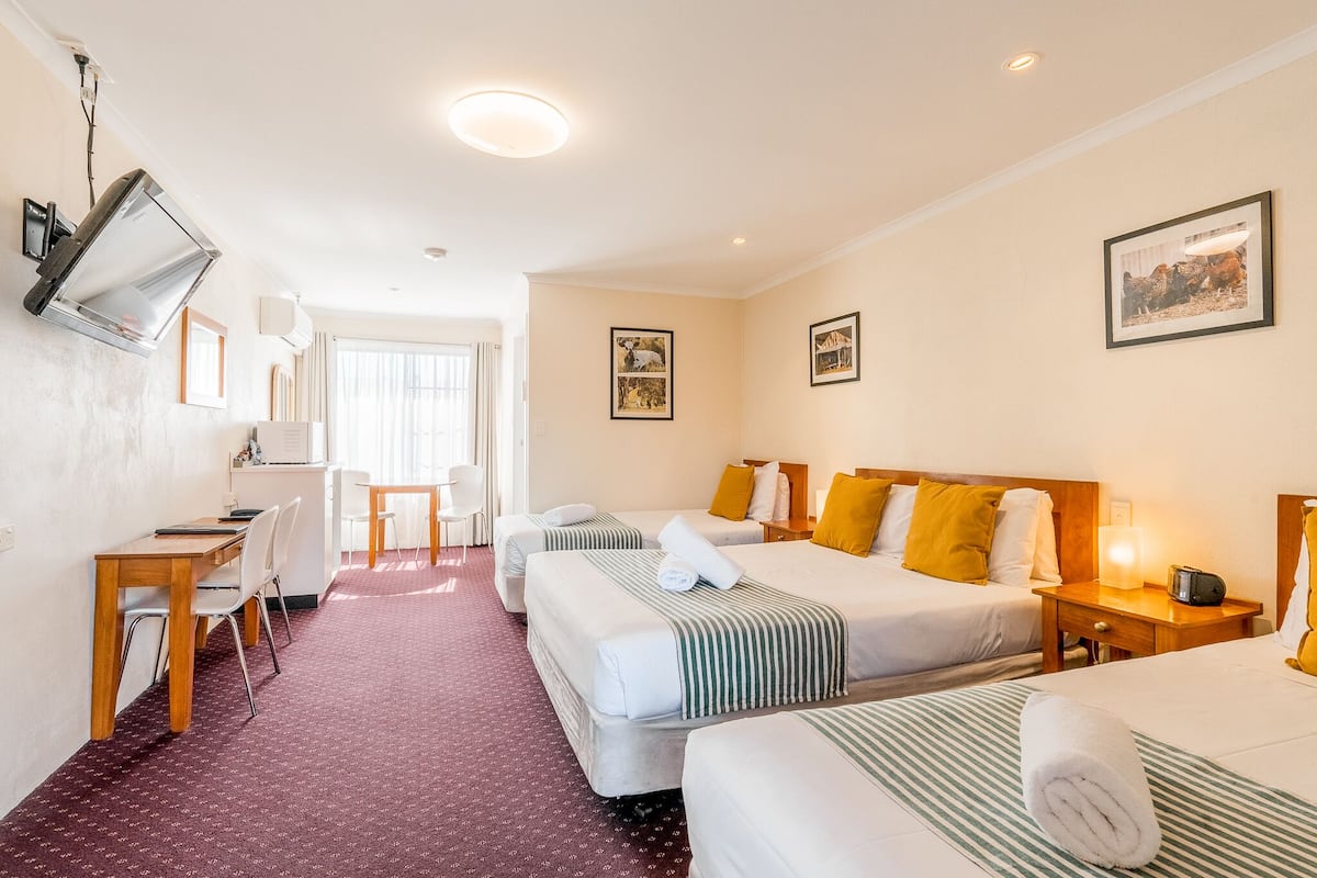 A hotel room with two single beds, a desk, a chair, a TV mounted on the wall, and a window with curtains.