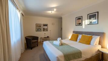 A hotel room with a large bed, a chair, a desk, and two framed pictures on the wall.