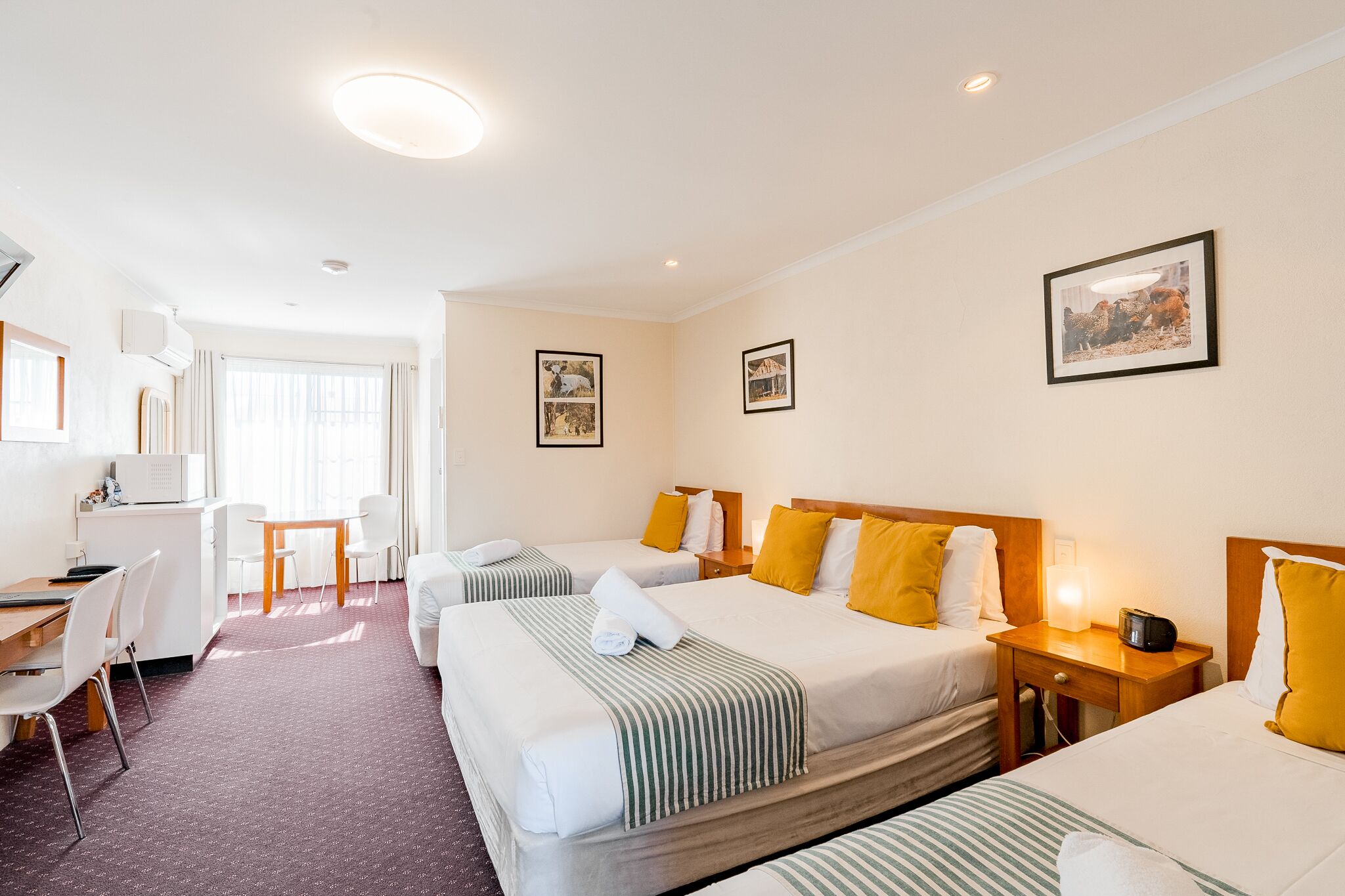 A hotel room with two beds, a desk, and a chair. There are pictures on the walls and a window with curtains.
