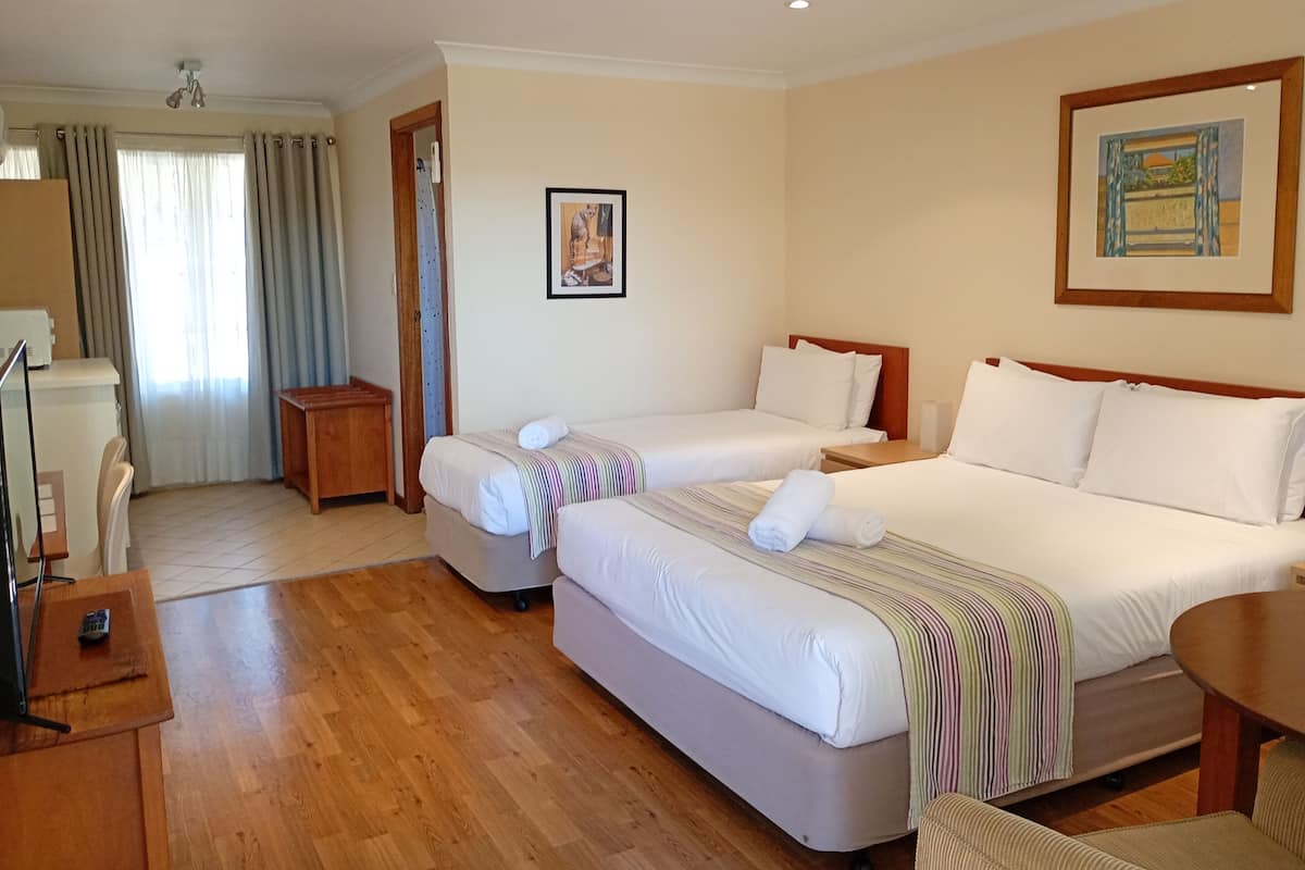 A hotel room with two beds, a desk, a chair, a small table, and a painting on the wall.