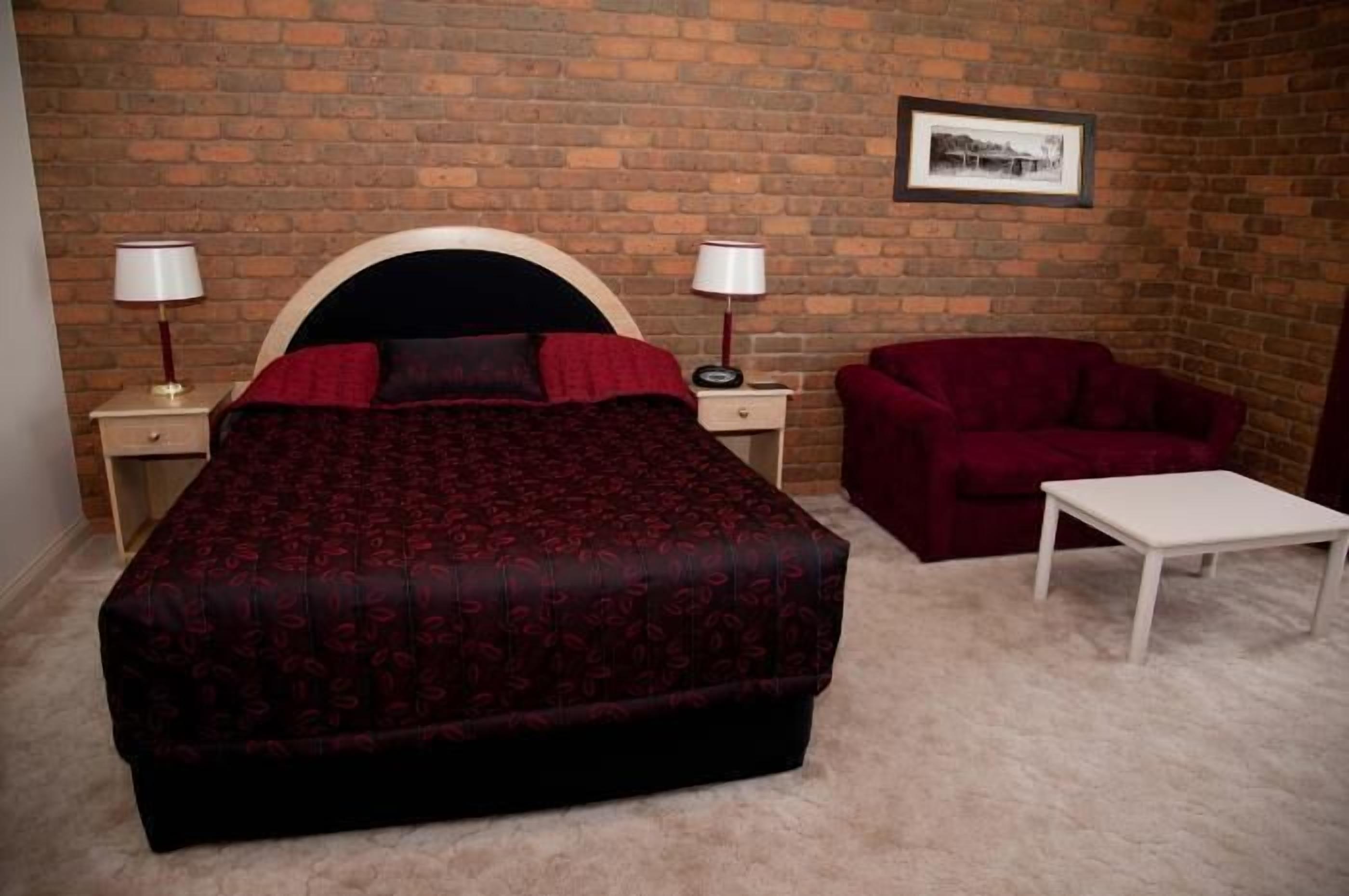 Ein Schlafzimmer mit einem großen Bett, zwei Nachttischen mit Lampen, einem roten Sessel und einem kleinen weißen Tisch.