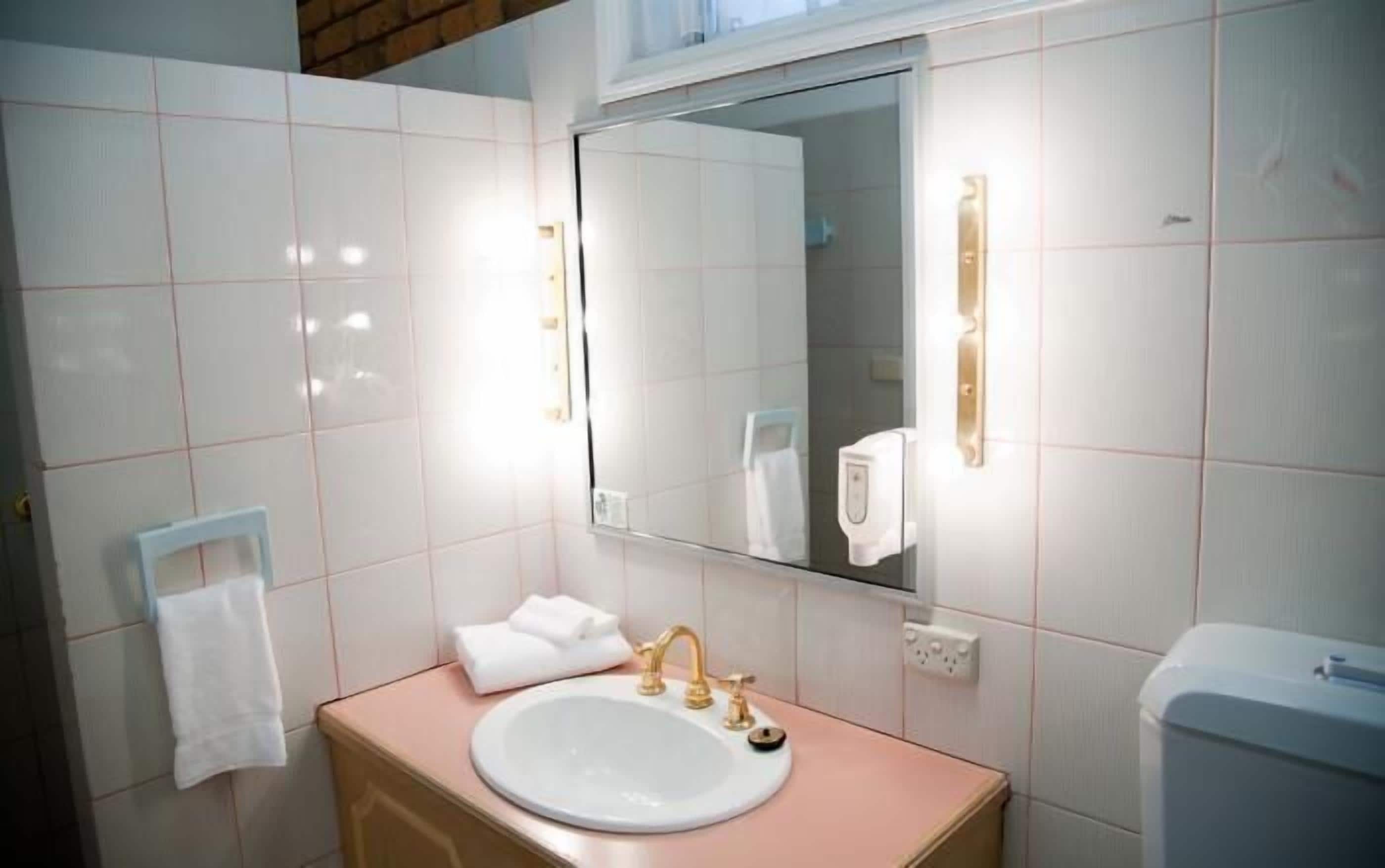 Un baño con azulejos blancos, un lavabo con grifo dorado, un espejo y un perchero para toallas.