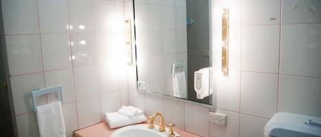 Un baño con azulejos blancos, un lavabo con grifo dorado, un espejo y un perchero para toallas.