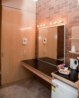 A room with a wooden wardrobe, a mirror with lights, a small table with snacks, a kettle, and a coffee machine.
