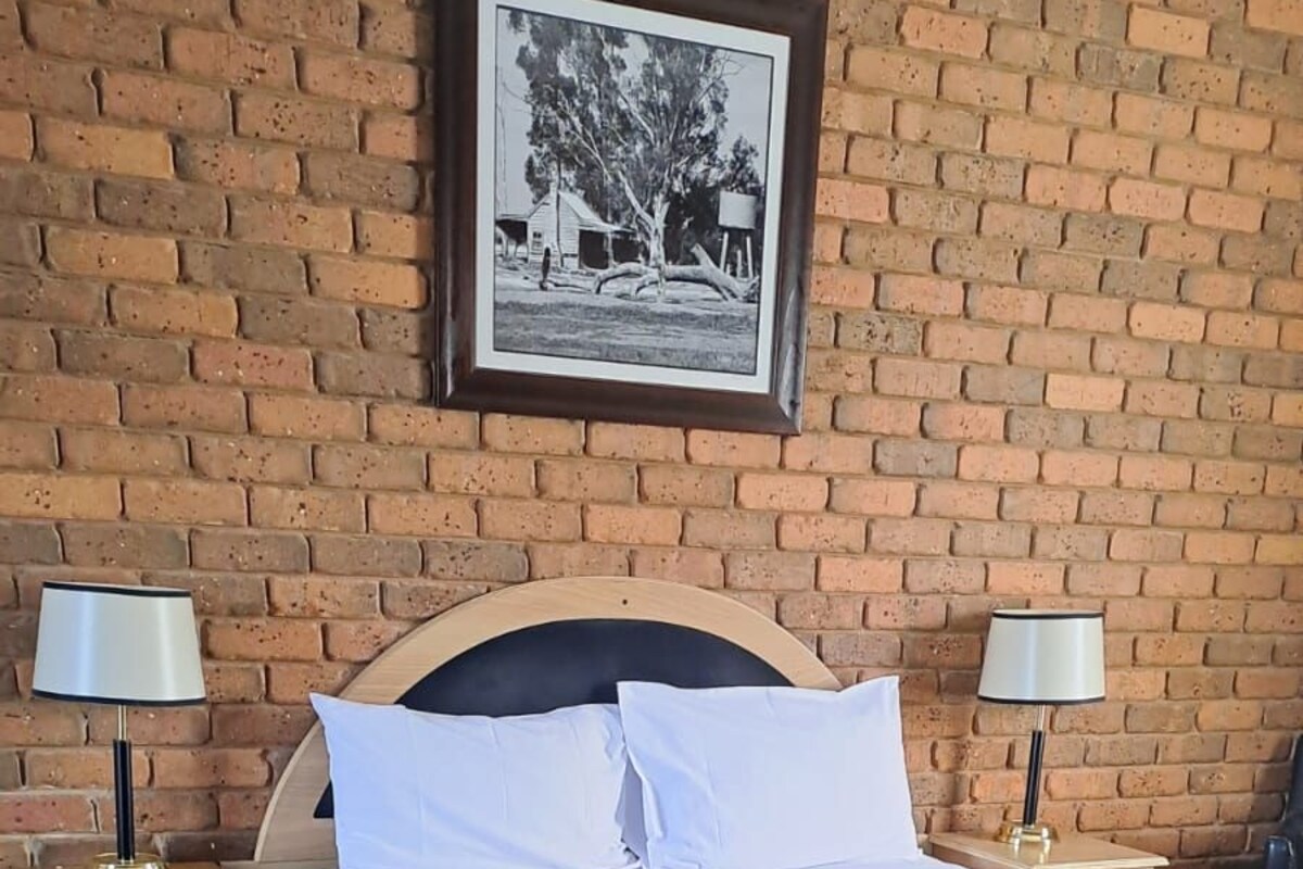 Una cama bien hecha con un colchón estampado, dos mesitas de noche con lámparas y un cuadro en la pared de ladrillo.