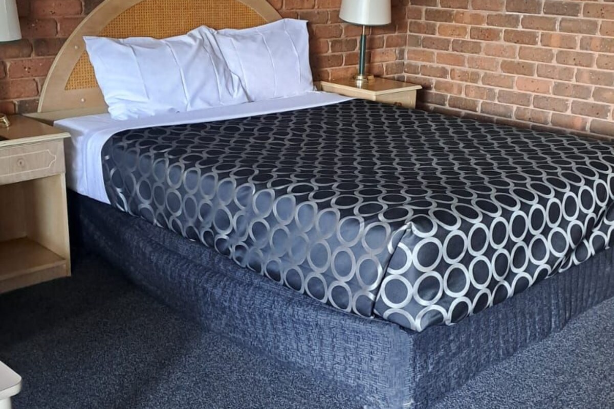 Una cama bien hecha con una colcha estampada, un cabecero de madera y dos lámparas de noche.
