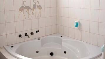 A bathroom with a large bathtub, white tiles, a brick wall, and a window.