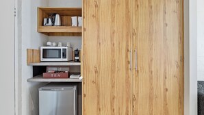 Une cuisine compacte équipée d’un micro-ondes, d’un grille-pain et d’une machine à café placés sur une étagère, et d’un réfrigérateur situé en dessous.