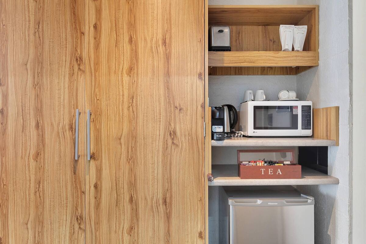 A wooden cabinet with a microwave, a tea box, and a small appliance on the shelf.