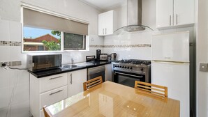 Une cuisine moderne avec des meubles blancs, un plan de travail noir, une cuisinière et une table à manger avec des chaises.