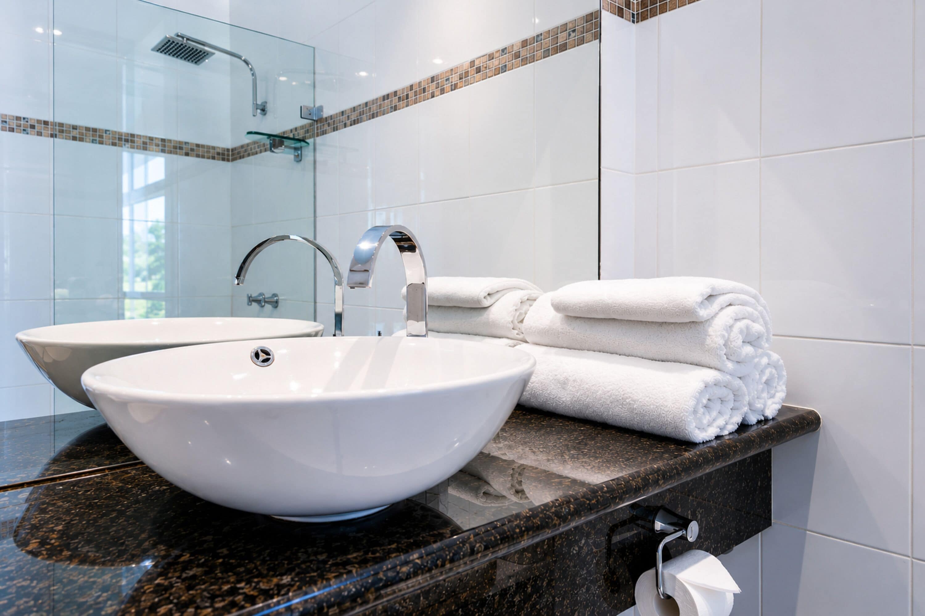 Een badkamer met een groot wit wastafelblad, een douchecabine van glas en een marmeren aanrecht.