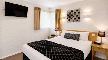 A hotel room with a bed, bedside tables, a flat-screen TV, and a window with curtains.