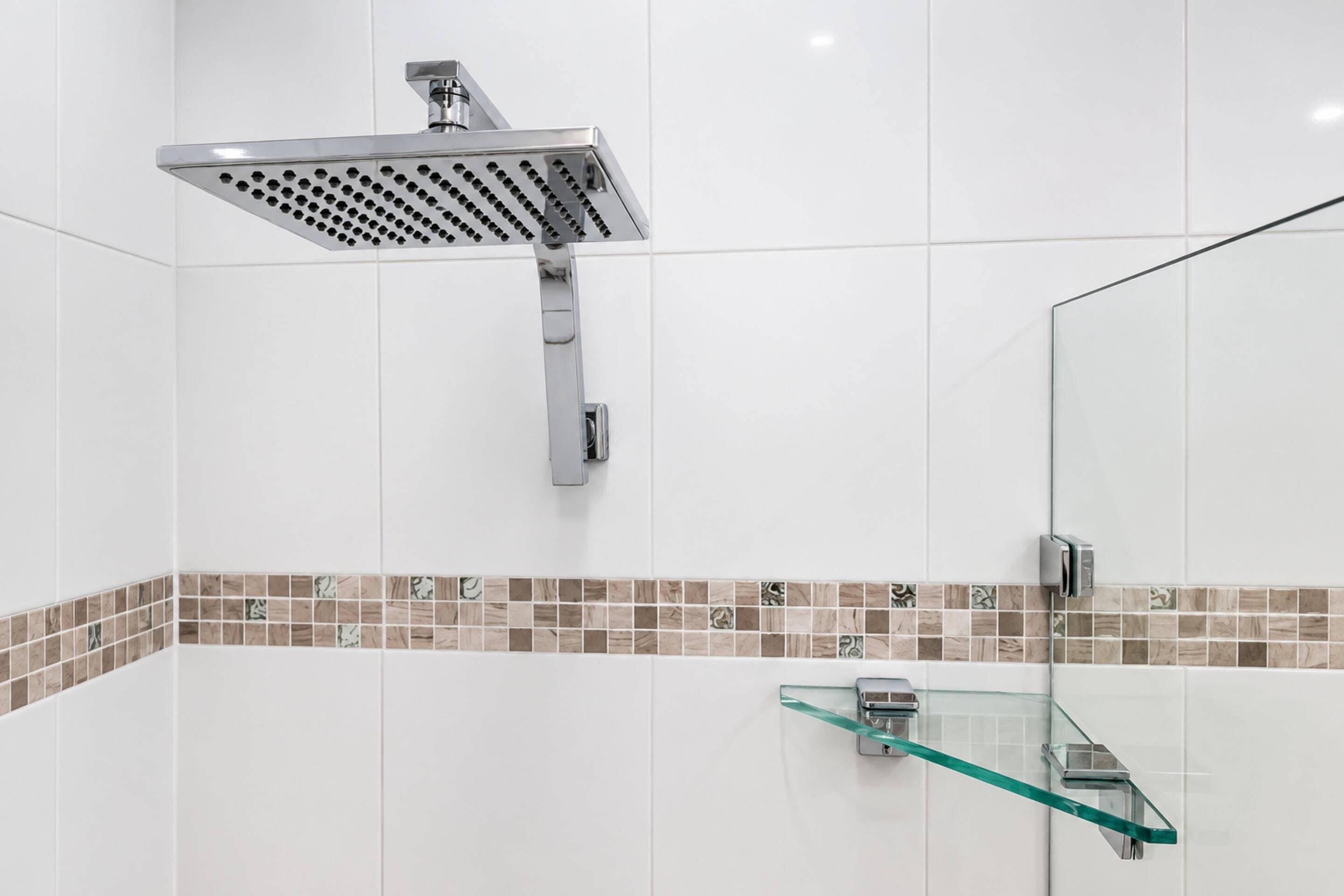 A modern bathroom with a shower, a glass shelf, and a tiled backsplash.
