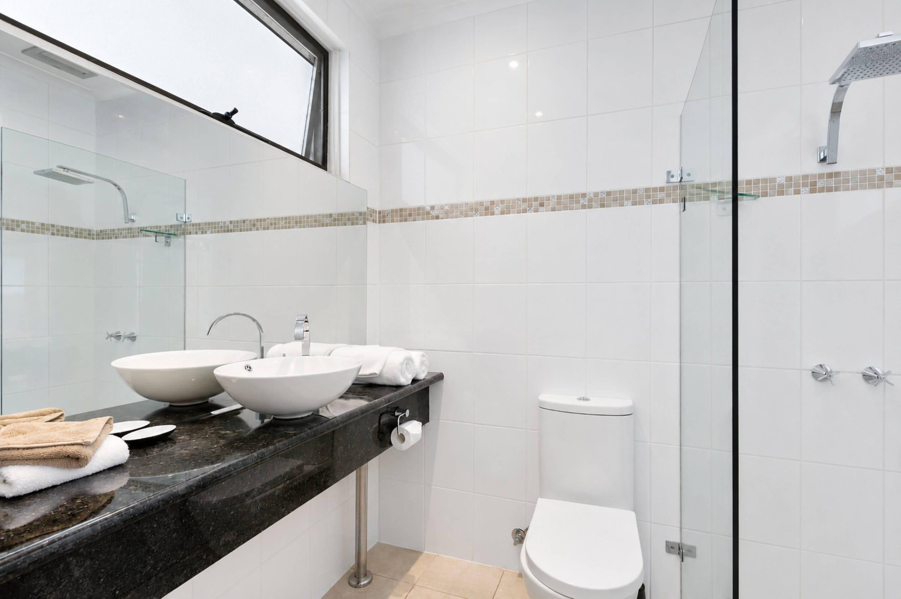 A modern bathroom with two vessel sinks, a glass shower enclosure, and a toilet.