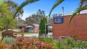 Un hôtel Comfort Inn doté d’une façade en briques, d’un espace extérieur aménagé avec des sièges et d’un jardin paysager agrémenté de diverses plantes et fleurs.