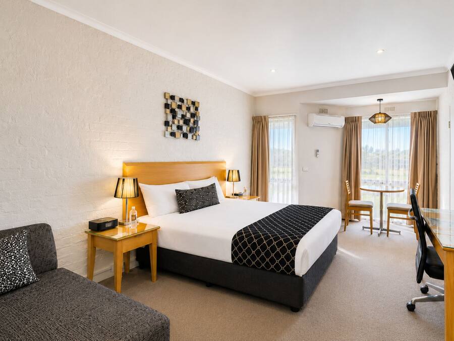 A hotel room with a bed, bedside tables, a desk, a chair, a TV, and a window with curtains.