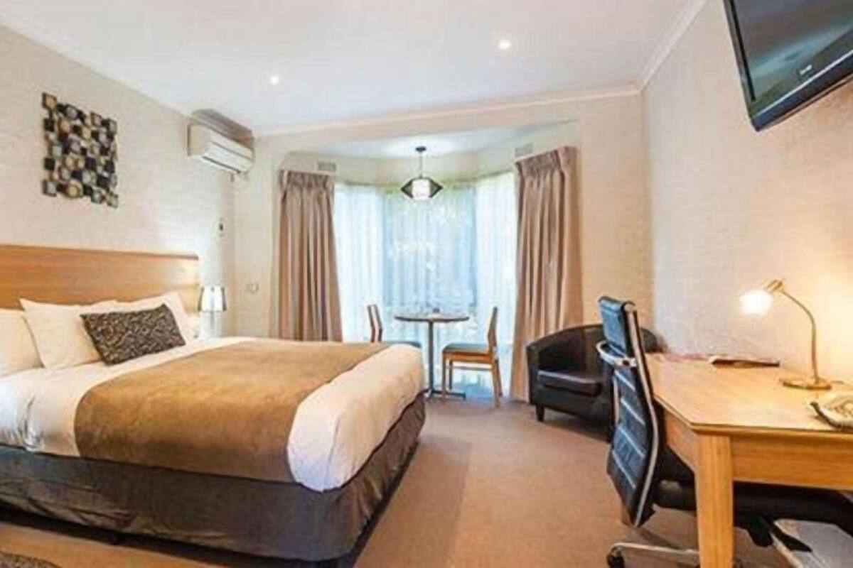 A hotel room with a large bed, a desk, a chair, a TV, and a window with curtains.