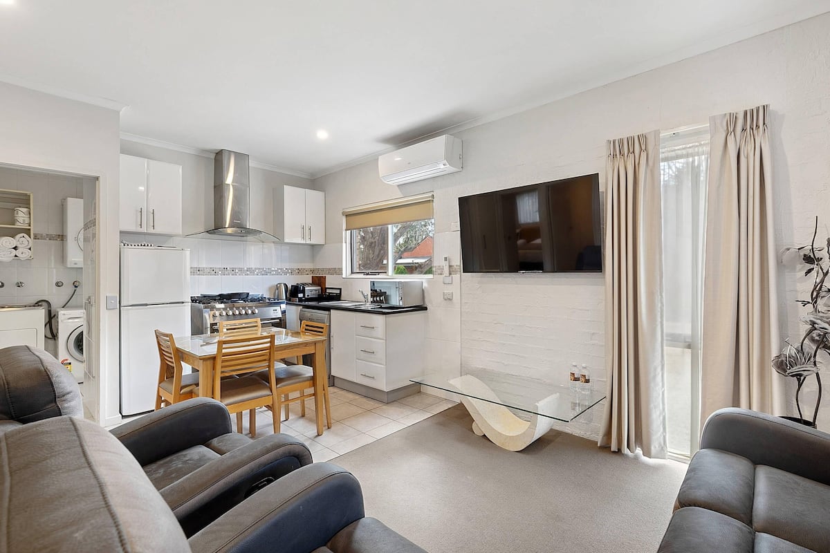 A modern kitchen with a dining area, a TV, and a glass coffee table.