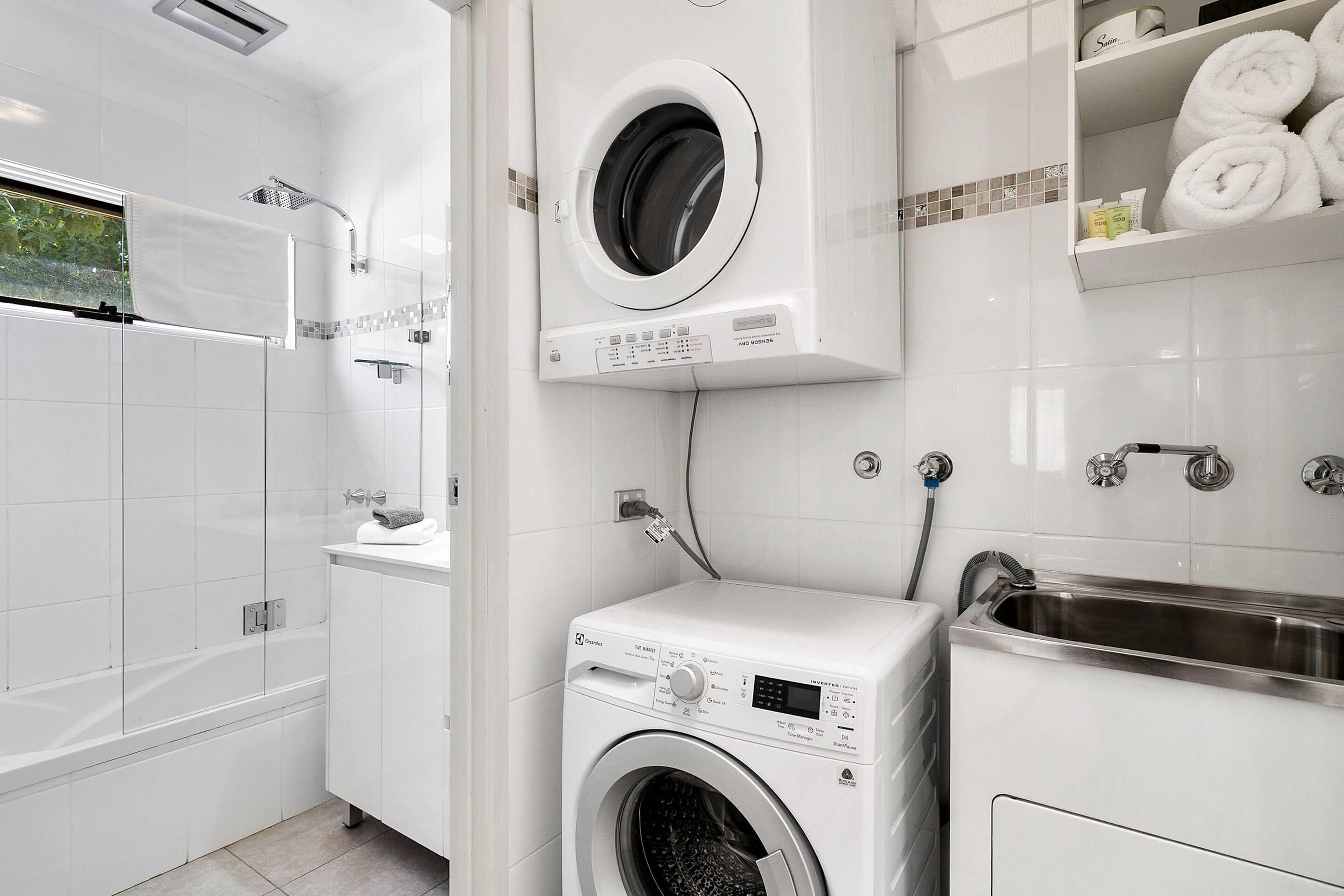 A modern bathroom with a built-in washer and dryer, a shower, and a sink.