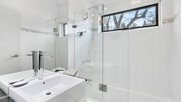 A modern bathroom with a large white sink, a glass shower enclosure, and a window with a view of trees.